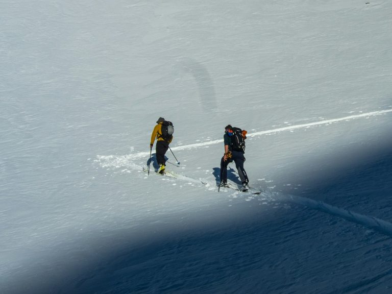 a couple of people riding skis down a snow covered slope